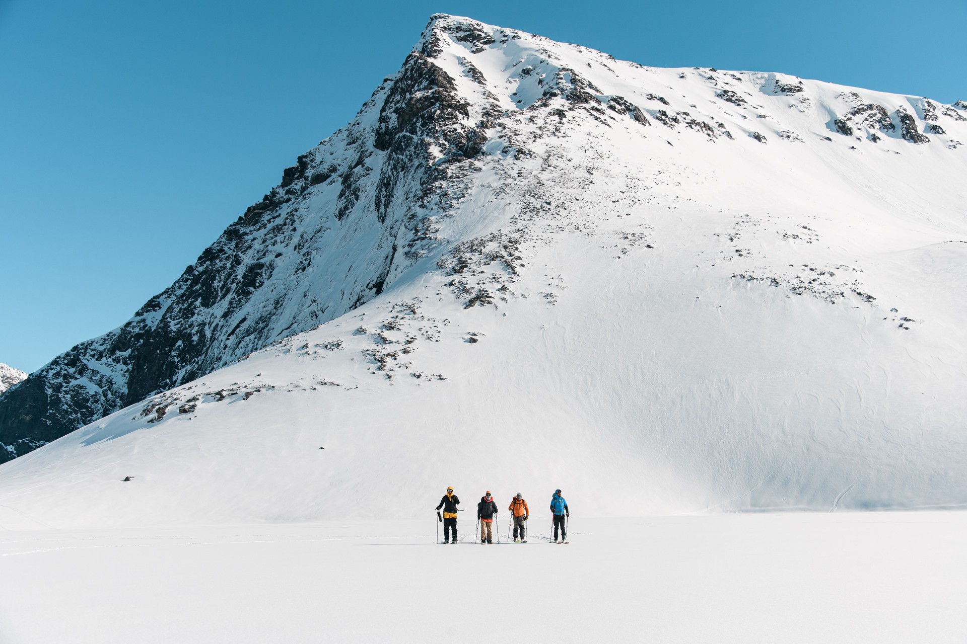 Four skier friends are skiing in a row side by side on smooth snow, one of them is one-handed